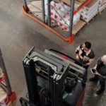 two warehouse workers standing next to a forklift looking to their right