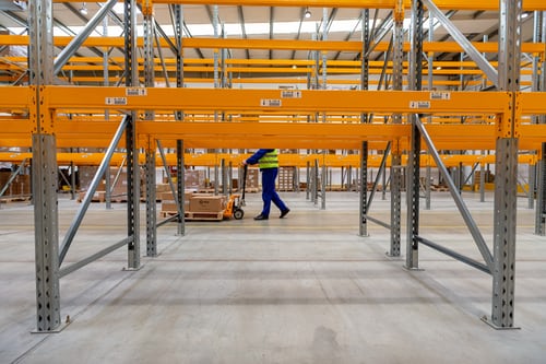 man pushing forklift behind empty racks