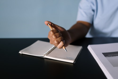 person sitting at desk with hand holding and clicking pen over blank notebook