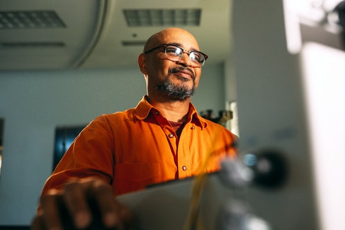 man with glasses wearing orange shirt sitting in front of computer