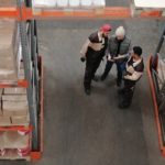 three workers standing and talking between aisles in a warehouse