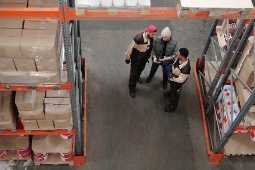 three workers standing and talking between aisles in a warehouse