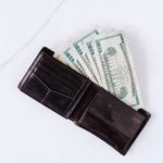 leather wallet sitting on table with four twenty-dollar bills coming out of it