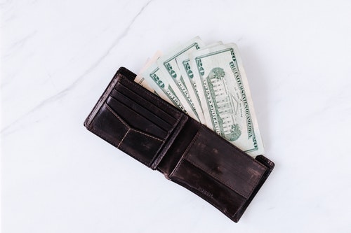 leather wallet sitting on table with four twenty-dollar bills coming out of it